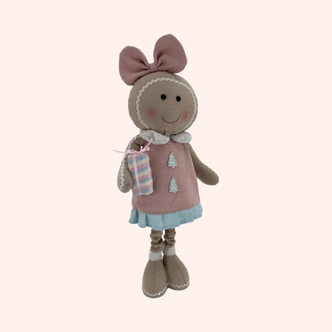 A plush gingerbread doll wearing a pink dress with a blue skirt, a pink bow on its head, and holding a small wrapped gift.