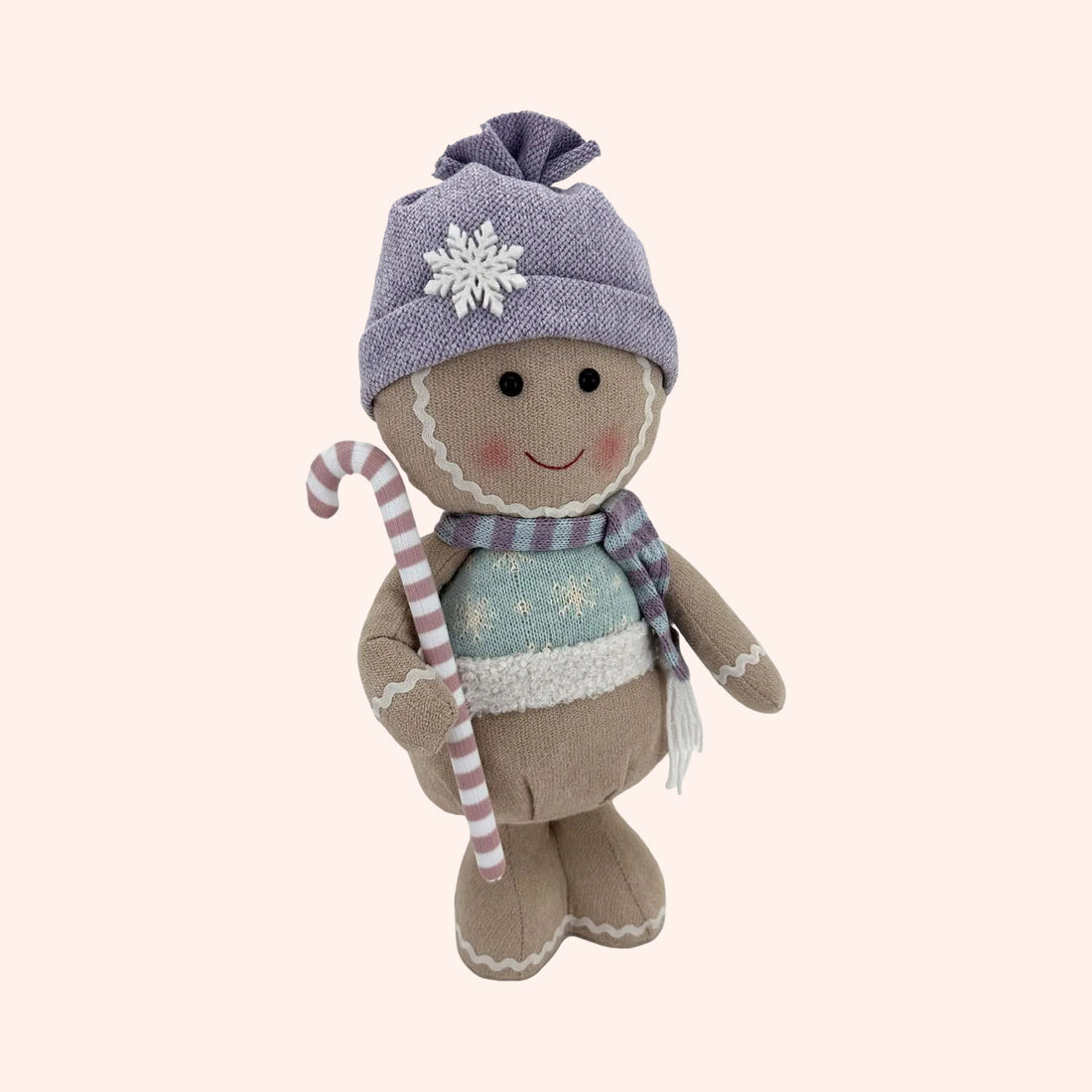 A gingerbread doll plush toy wearing a lavender knit beanie with a white snowflake, a blue patterned scarf, and holding a pink and white striped candy cane, set against a plain background.