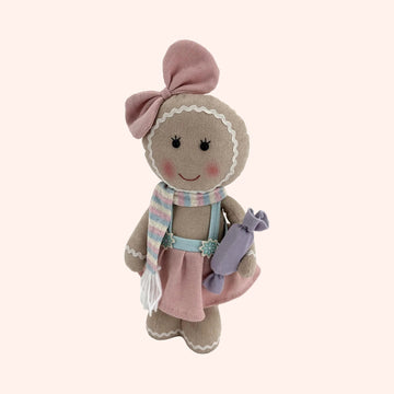 A soft fabric gingerbread doll with a pink bow, pastel striped scarf, and pink skirt, holding a purple candy, isolated on a plain background.