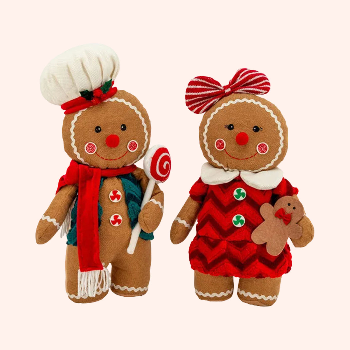 Two Christmas gingerbread doll plush toys on a plain background. One male doll wears a white chef hat, a red scarf, and holds a lollipop. One female doll wears a bow, a red chevroned dress, and holds a gingerbread man.