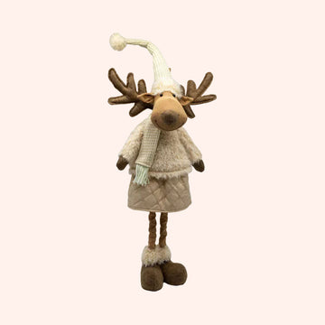 A plush moose decoration wearing a cream knit hat with a pom-pom, a cream sweater, a quilted beige skirt, and brown antlers, photographed on a plain background.